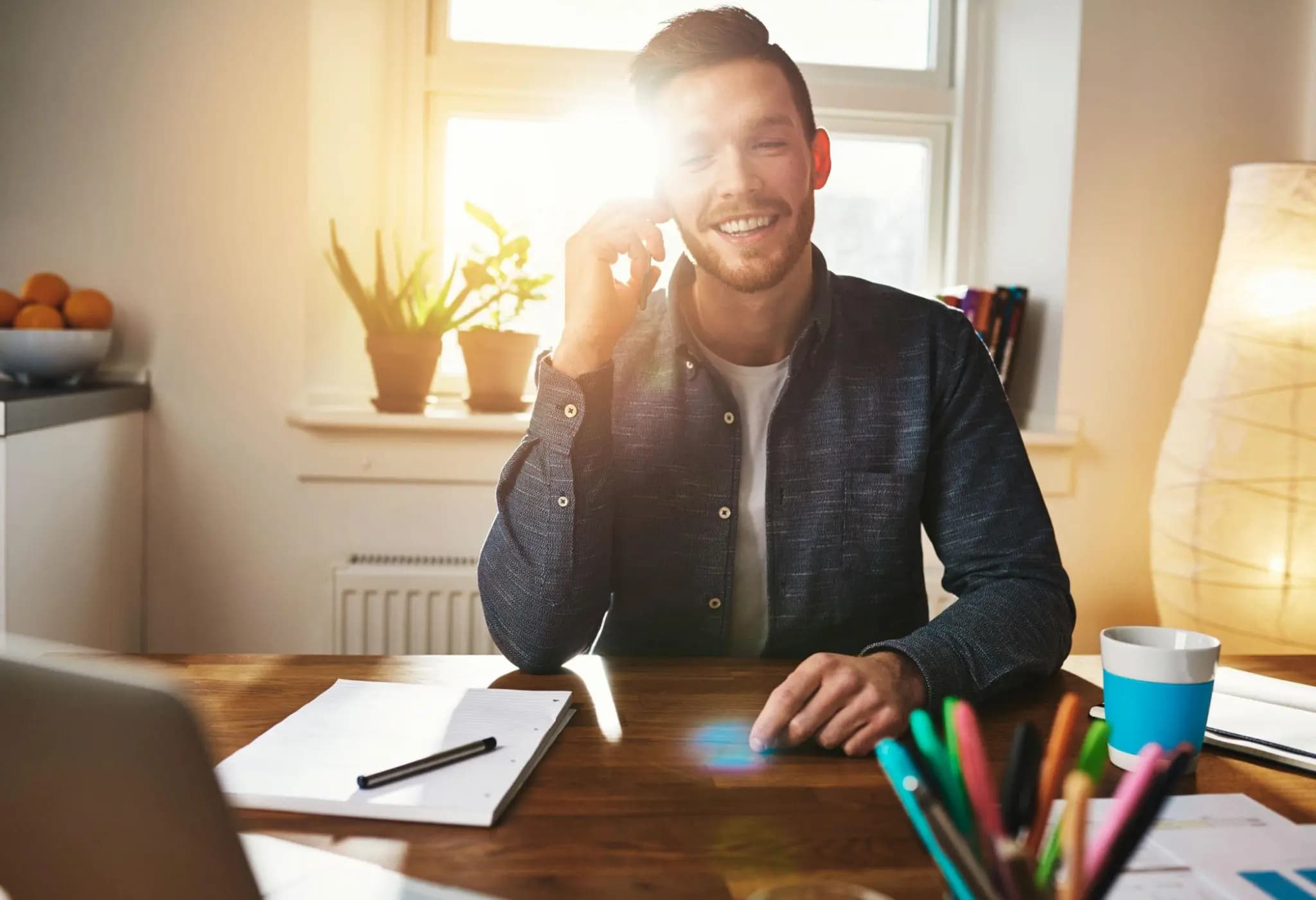 Smiling entrepreneur in a sunlit home office talking on his phone to complete a Florida DBA registration.