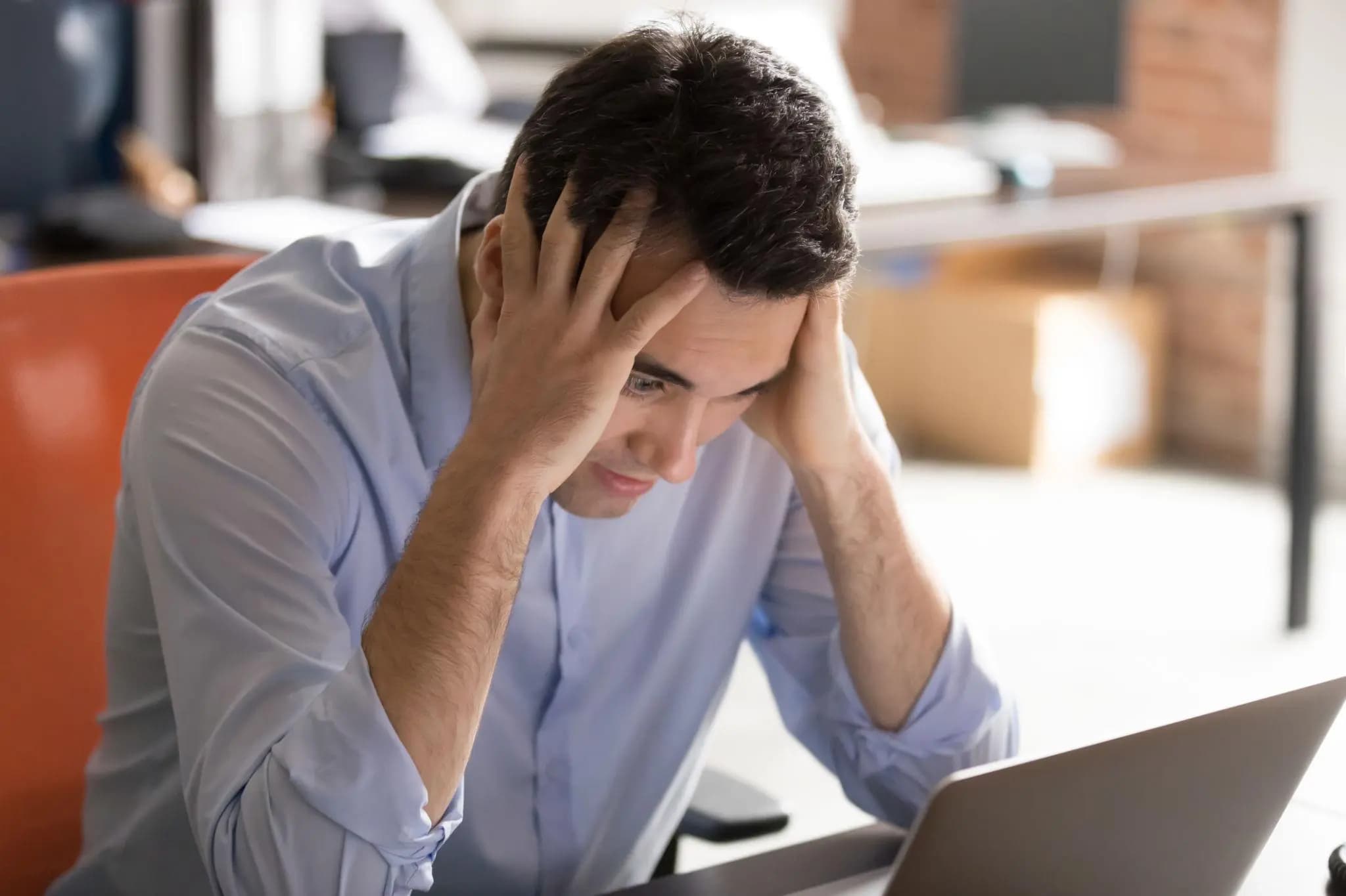 Stressed entrepreneur holding his head while staring at a laptop, needing to reinstate Florida LLC.
